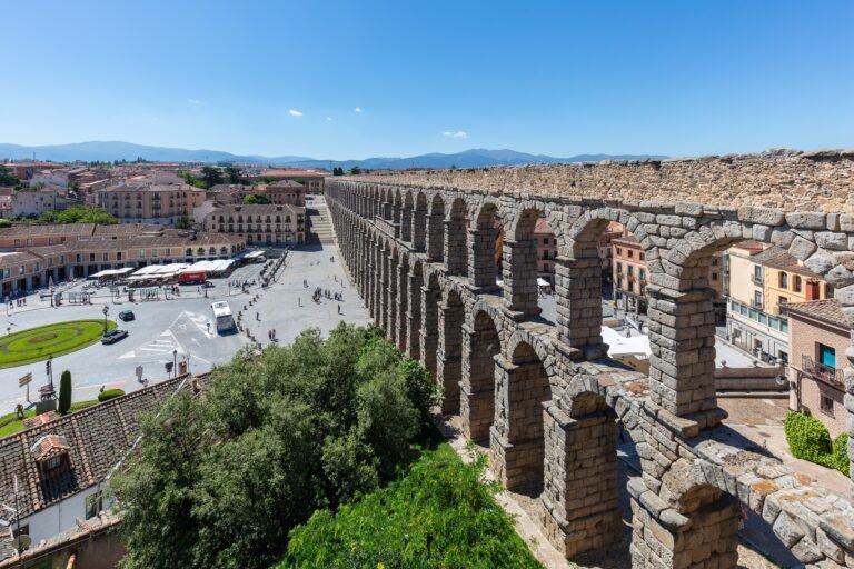 Vista elevada dos arcos e blocos de granito do Aqueduto de Segóvia, com a cidade ao fundo