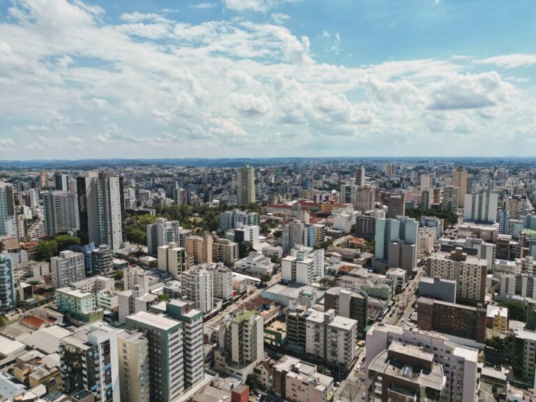 Vista aérea de Caxias do Sul, com edifícios e áreas urbanas sob o céu azul.