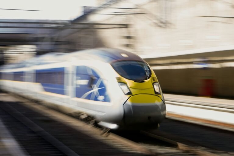 Trem Eurostar azul e amarelo em movimento junto a uma plataforma.