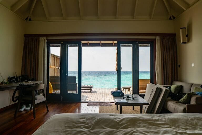 Quarto com cama, poltronas e varanda aberta para o mar.