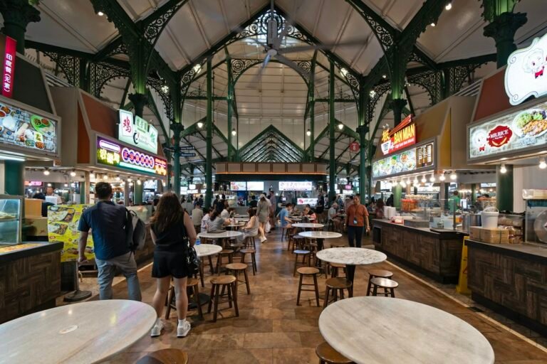 Mesas e bancas de comida no interior do Lau Pa Sat, sob a estrutura metálica verde do mercado em Singapura.