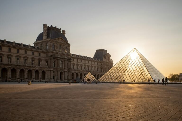 Pirâmide de vidro e fachada histórica do Museu do Louvre ao entardecer, em Paris