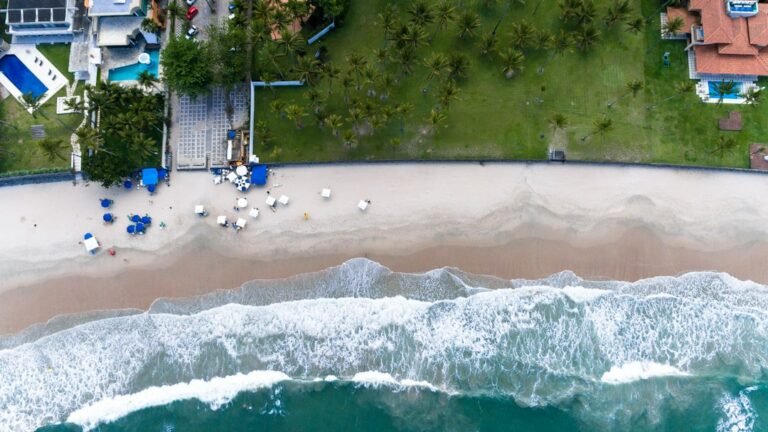 Vista aérea de praia em Guarujá, com faixa de areia, guarda-sóis e ondas