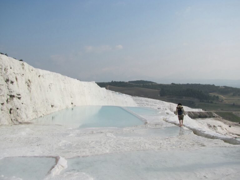 Terraços brancos de Pamukkale com água azul-clara e um visitante visto de costas